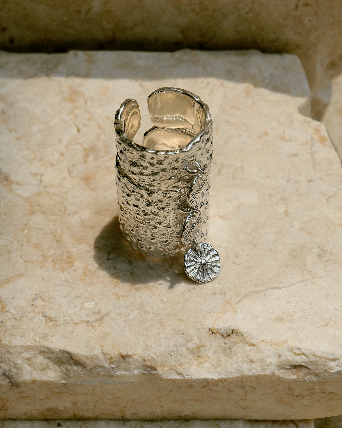 Elegant silver ring with a hammered texture and a flower-shaped charm, designed for nature lovers and photographed on natural stone