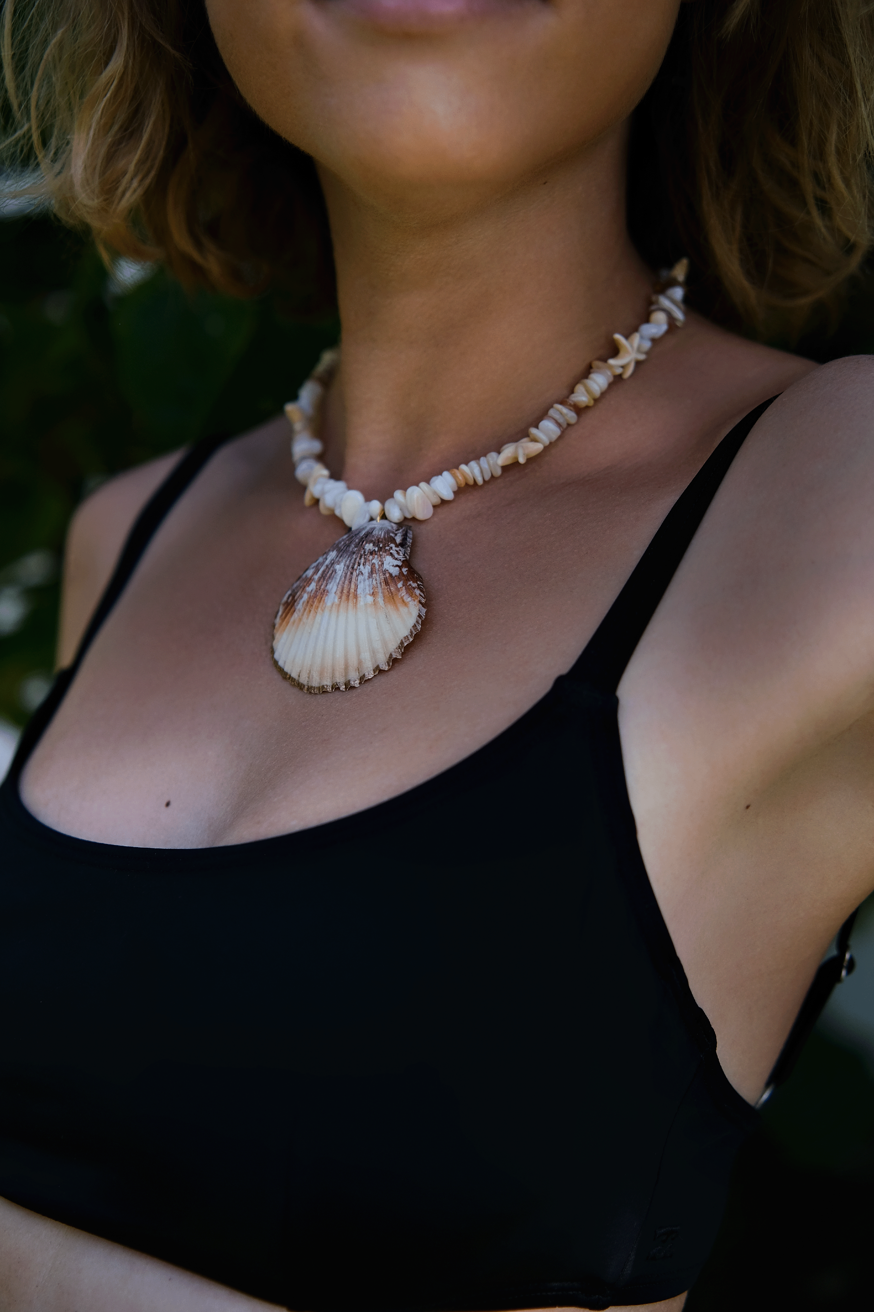 Close-up of a woman wearing a bohemian shell necklace with a natural seashell pendant, perfect for beach-inspired fashion and coastal jewelry lovers